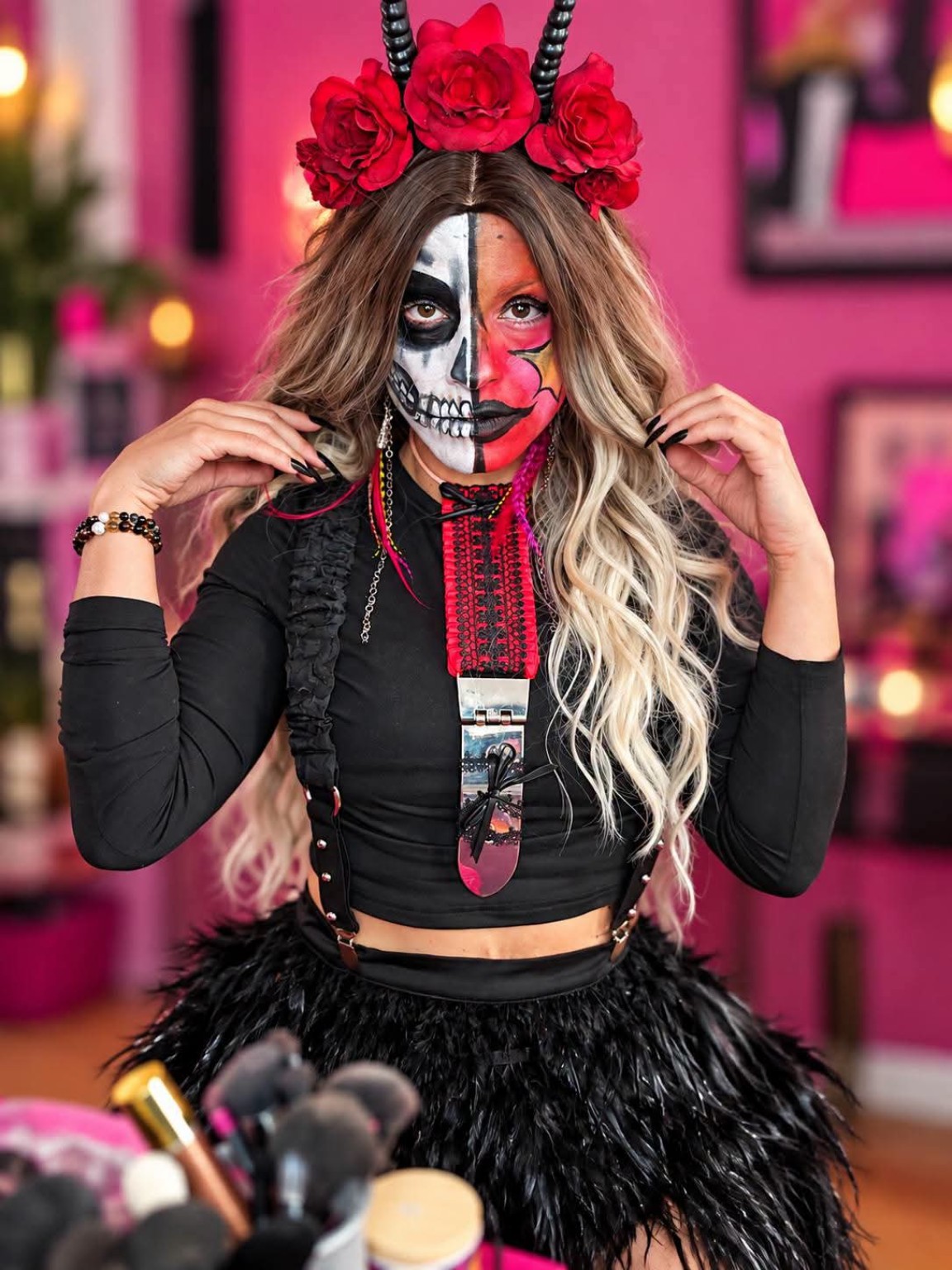 Visage partagé entre squelette noir et blanc et maquillage pop rouge et rose au motif jaune, avec cheveux blonds et bruns, roses rouges, cornes noires et tenue noire.